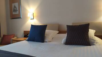 A neatly made bed with white linens and two pillows, a bedside table with a phone, and a wall-mounted light fixture.