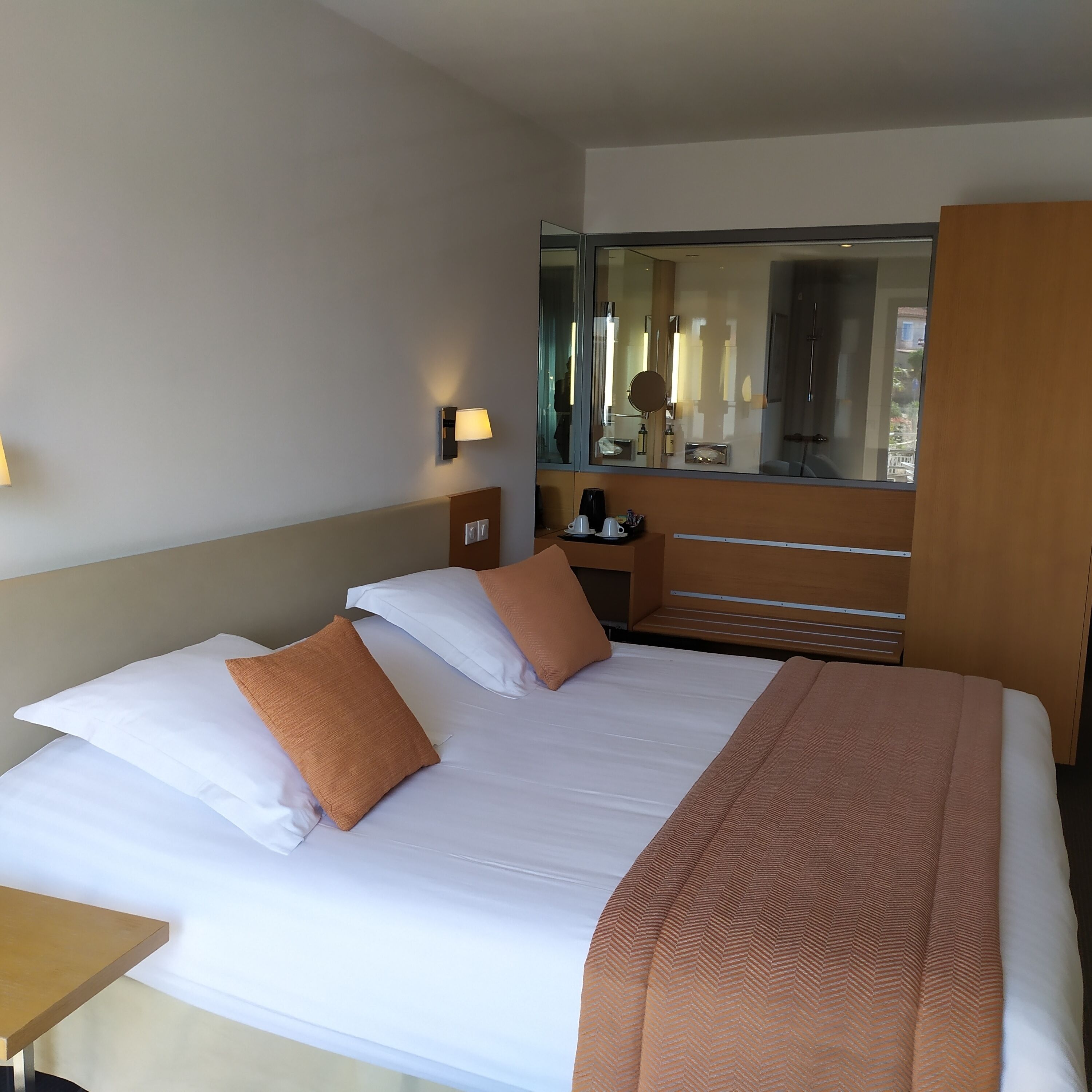 Quarto de hotel com uma cama grande, uma mesa de cabeceira, um espelho e uma janela com vista para edifícios.