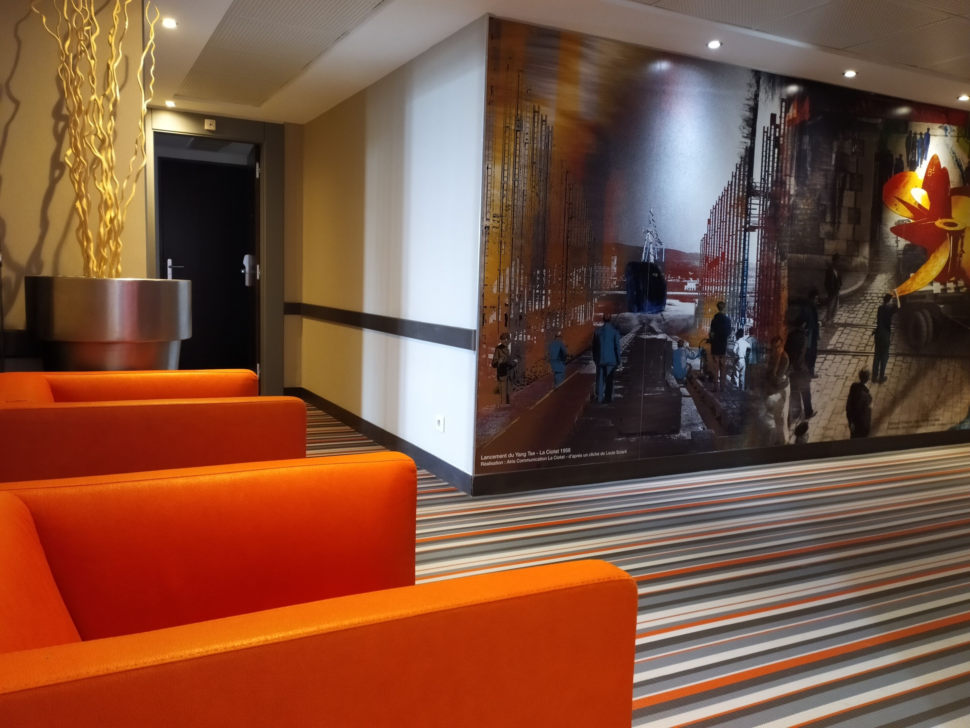 Vestíbulo de hotel con asientos naranja, un gran mural y un diseño de techo moderno.
