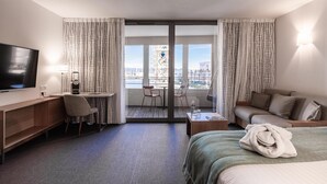 Una habitación de hotel con cama, escritorio, televisión, balcón y vistas a la ciudad, además de un sofá.