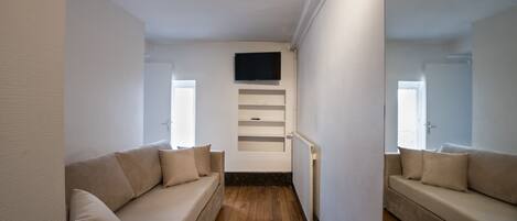A modern living room with a beige sofa, a flat-screen TV mounted on the wall, and a wooden floor.
