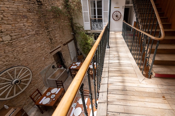 A wooden staircase with a railing leading to a dining area with tables set for four. - Hôtel des Tonneliers  (Beaune)