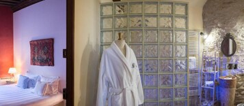 Habitación de hotel con una cama, una bata colgada en un perchero y un baño con un espejo y estantes.