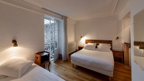 A hotel room with two beds, a wooden floor, a window with curtains, and a radiator. - Hôtel des Tonneliers  (Beaune)