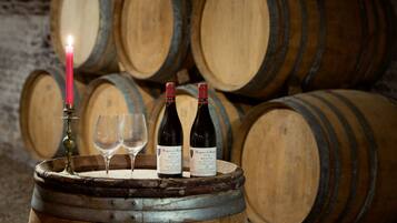 Dos botellas de vino y dos copas sobre un barril de madera, con una vela encendida en primer plano, frente a un fondo de barriles de madera apilados.