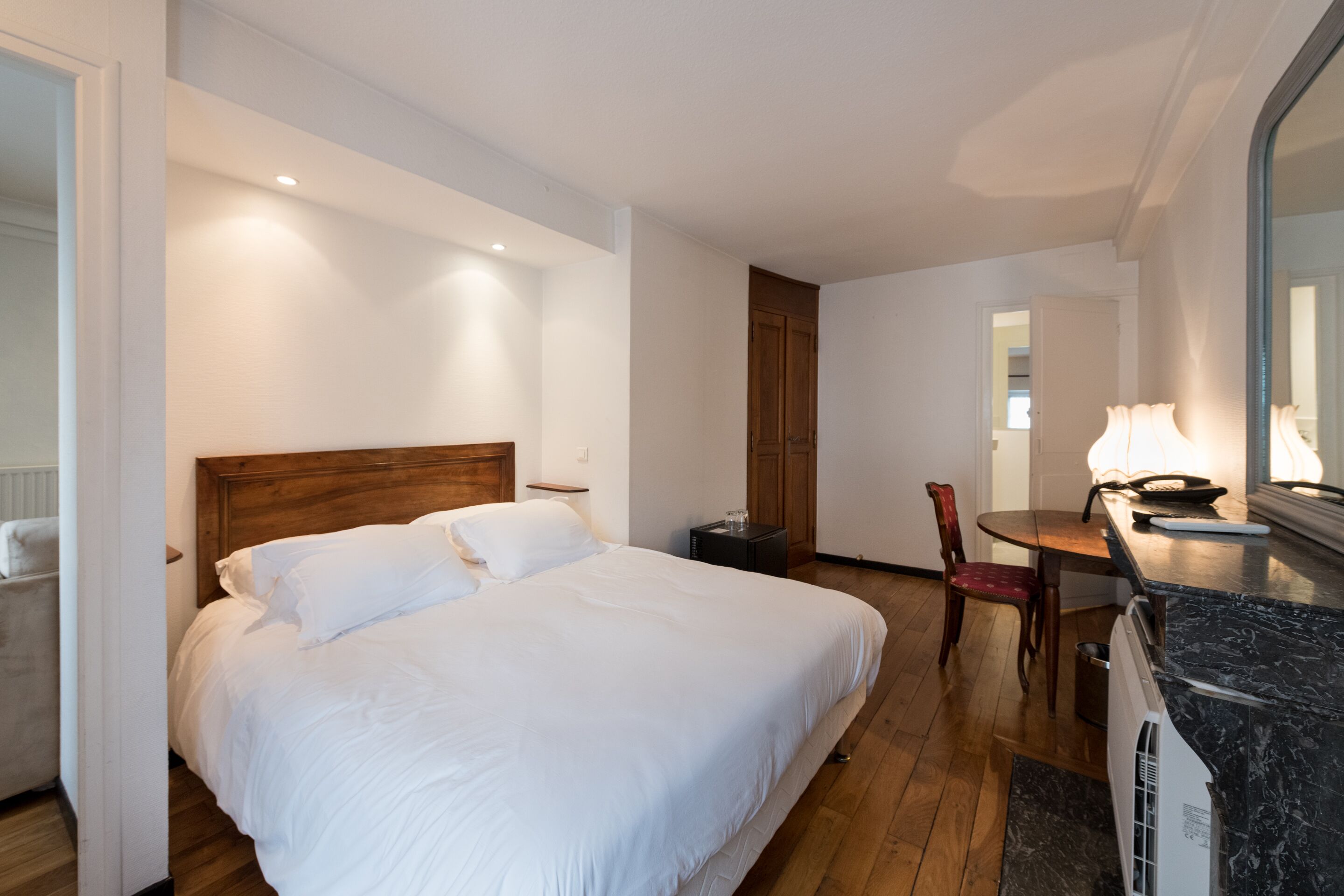 Une chambre d’hôtel avec un grand lit, une tête de lit en bois, une table à manger avec des chaises, une petite table d’appoint et un miroir au-dessus du comptoir.