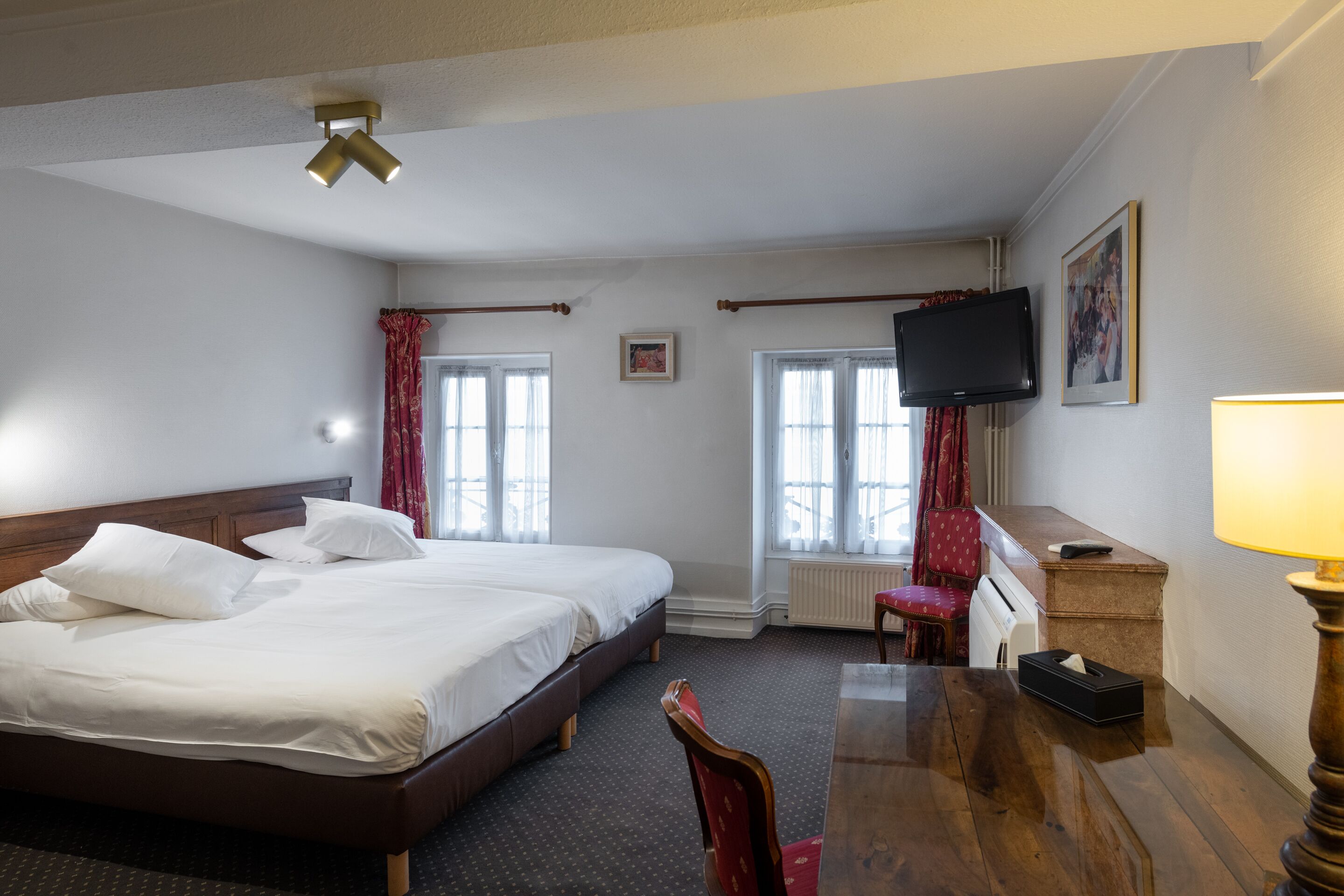 A hotel room with two beds, a desk, a chair, a television, and a window with curtains.