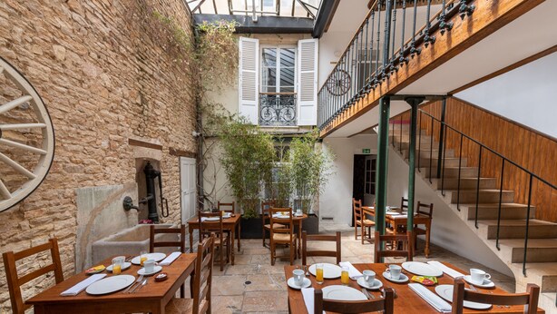 A courtyard with wooden tables and chairs set for dining, a stone wall, and a staircase leading to an upper level. - Hôtel des Tonneliers  (Beaune)
