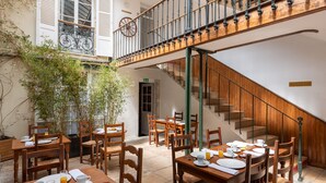 A dining area with wooden tables and chairs, a staircase, and a view of the outside. - Hôtel des Tonneliers  (Beaune)