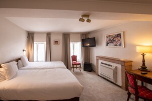 Habitación de hotel con dos camas, televisor, chimenea y escritorio con lámpara.