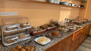 A buffet with various baked goods, including bread, pastries, and donuts, displayed on a granite countertop. - Palacio Congresos (Palencia)