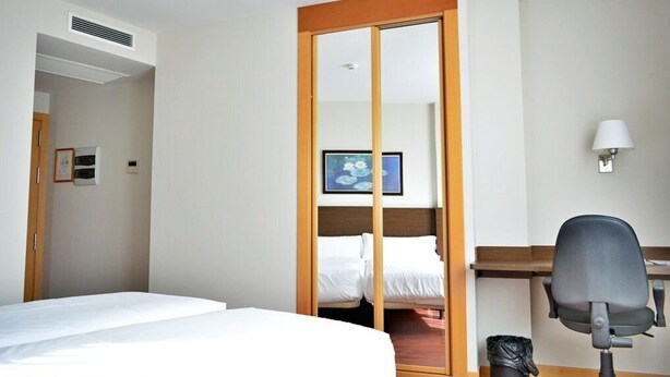 A hotel room with a bed, a desk, a chair, a TV, and a wardrobe. - Palacio Congresos (Palencia)