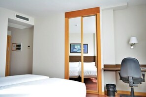 A hotel room with a bed, a desk, a chair, a TV, and a wardrobe. - Palacio Congresos (Palencia)