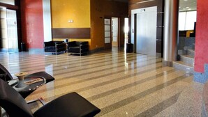 A spacious lobby with a check-in counter, seating area, and a staircase leading to an elevator. - Palacio Congresos (Palencia)