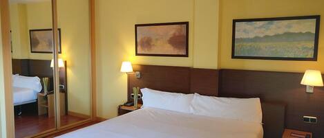 A hotel room with a large bed, two bedside tables with lamps, a mirror, and two framed artworks on the walls.