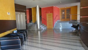A lobby with a staircase, a reception desk, and a seating area with chairs. - Palacio Congresos (Palencia)