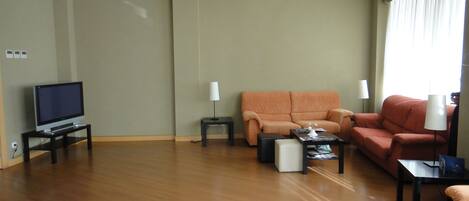 A modern living room with a flat-screen TV, two sofas, a coffee table, and a small side table.