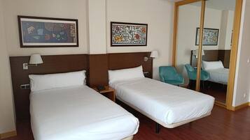 Habitación de hotel con dos camas individuales, suelo de madera, un espejo grande y dos sillas.