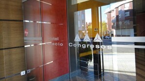 A hotel entrance with a glass door, a sign for 'Hotel Palacio Congreso', and a reflection of buildings and a street. - Palacio Congresos (Palencia)