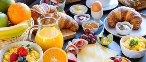 Una mesa con bollos, queso, frutas y bebidas para el desayuno.