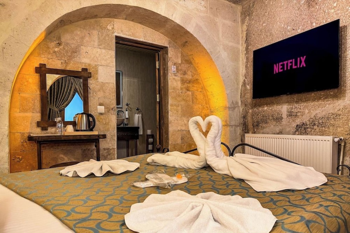 A hotel room with a bed, a television displaying 'NETFLIX,' and a stone wall.