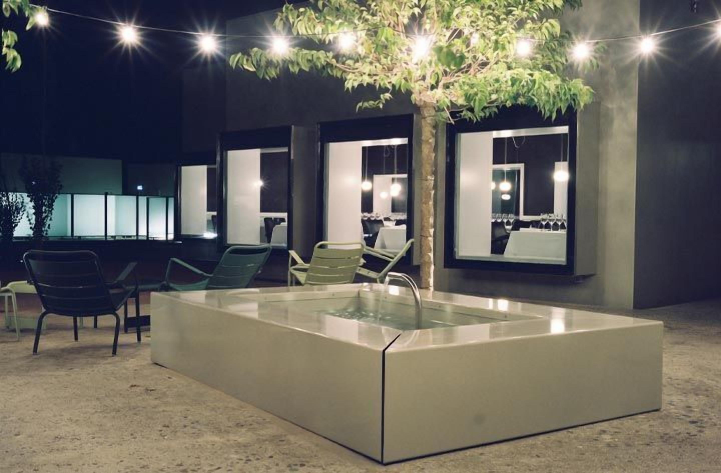 Zona de piscina interior moderna amb envàs de vidre, seients i llums penjants.