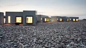 Een rij moderne, minimalistische hotelkamers met grote ramen en deuren, gelegen op rotsachtig terrein.
