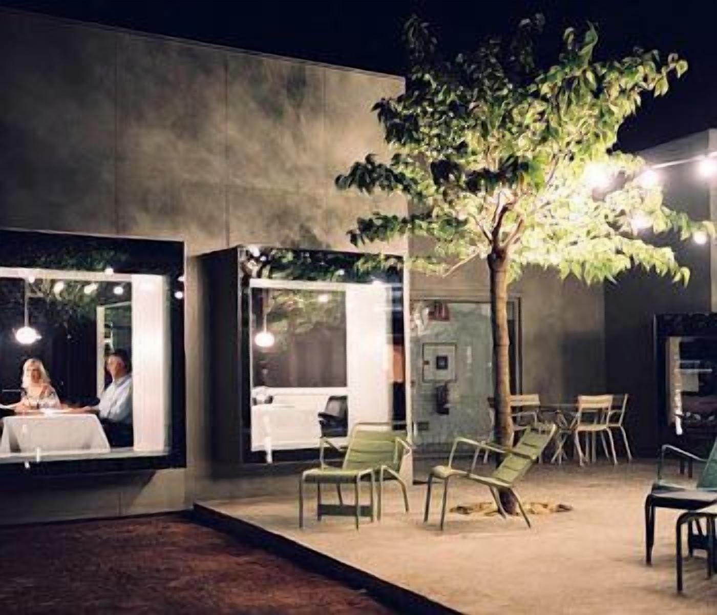 Un espace extérieur aménagé avec des tables et des chaises, un arbre et un bâtiment aux murs de verre.