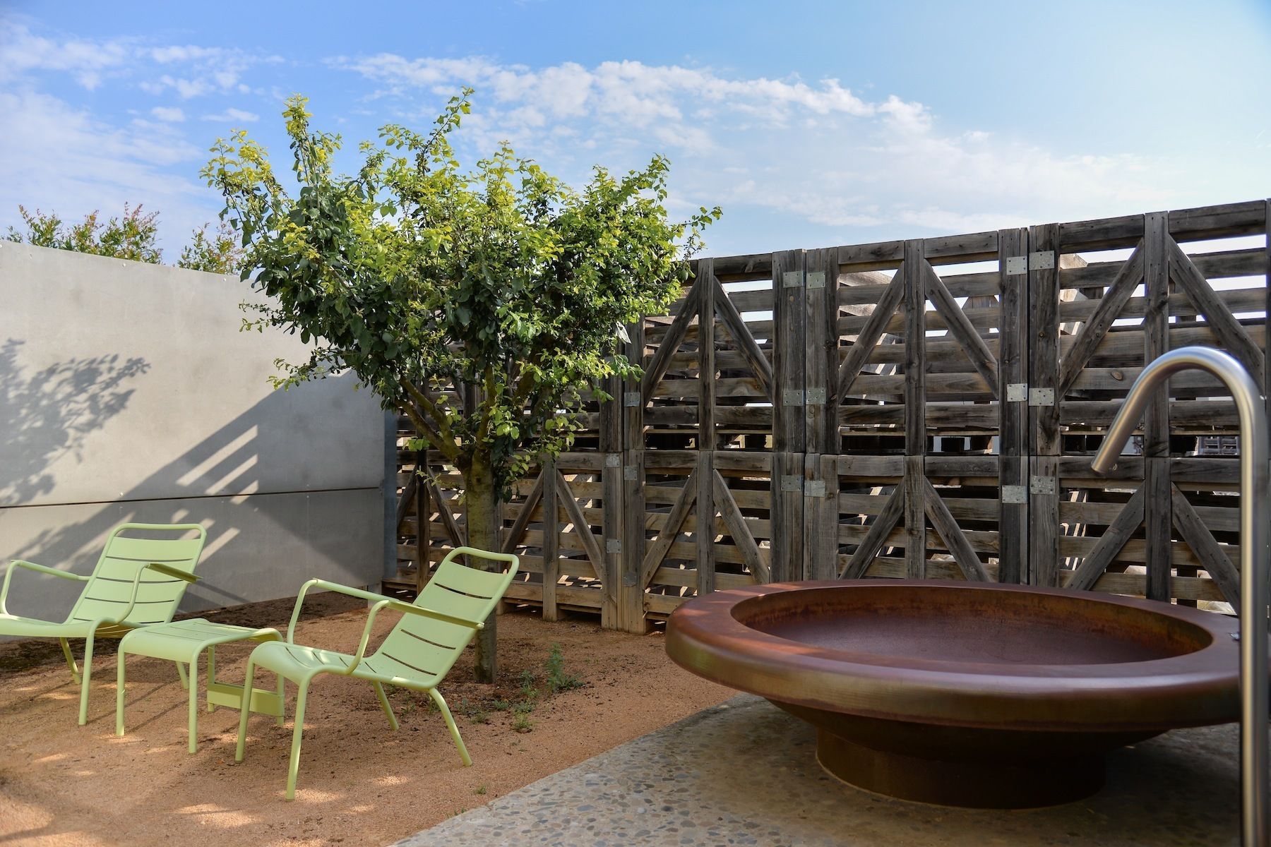 Un patio con dos sillas verdes, un recipiente metálico grande y una valla de madera.