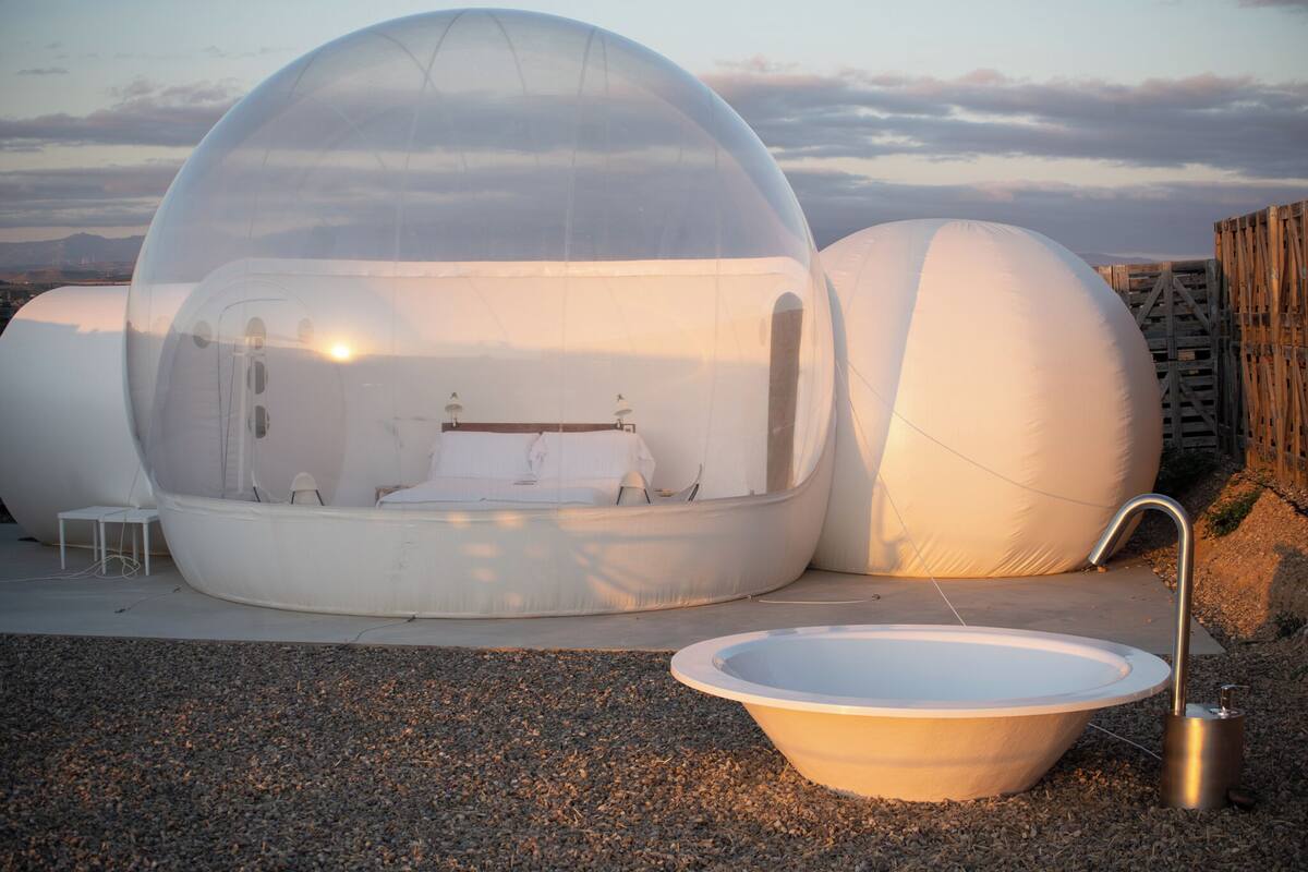 A spherical structure with a bed and a sink, set against a sunset backdrop.