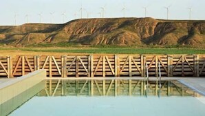 Zwembad met een houten omheining op de voorgrond en windturbines op de achtergrond.