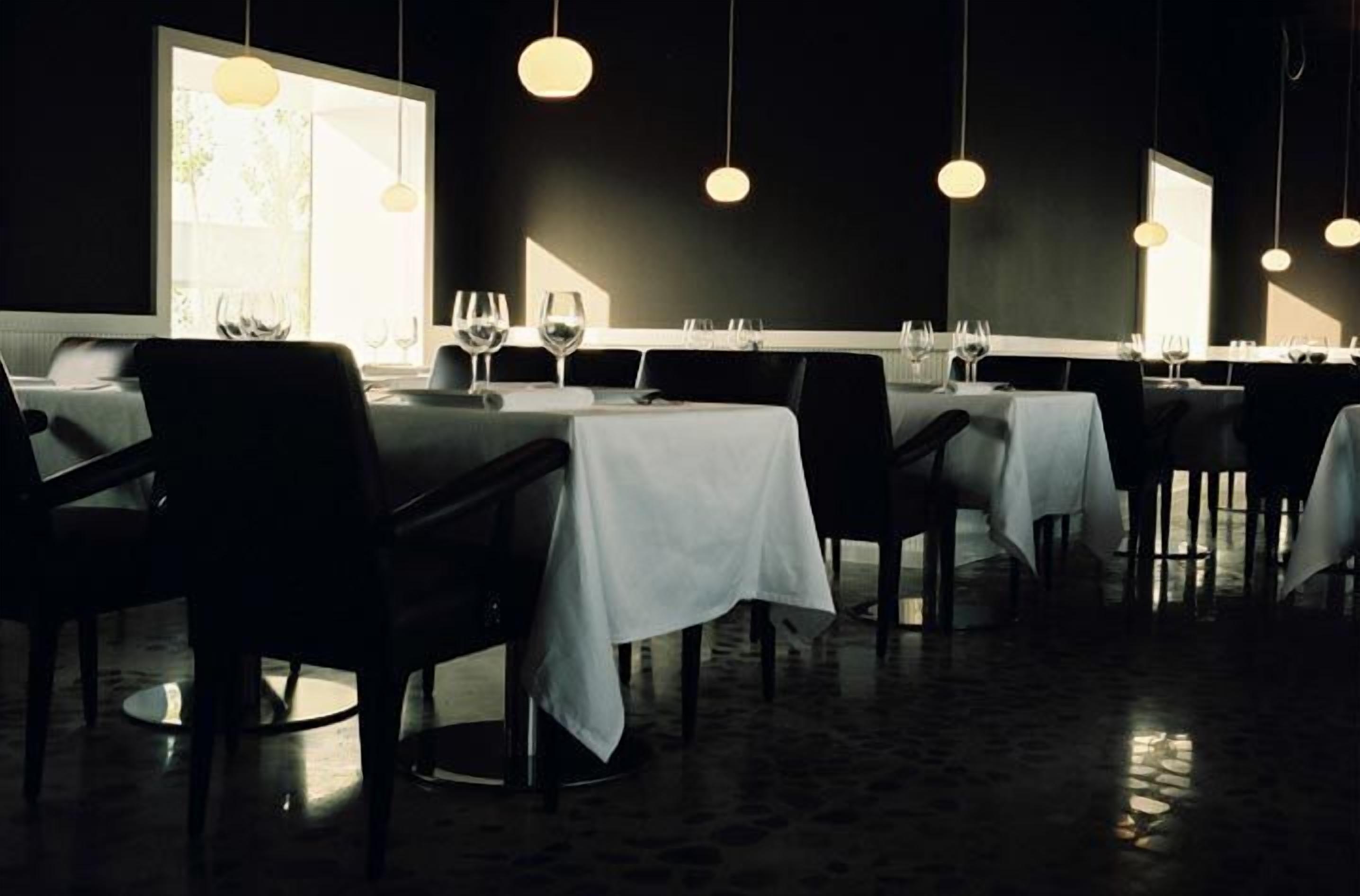 Een restaurant met gedekte tafels, verlichting boven de tafels en uitzicht op het omliggende landschap.