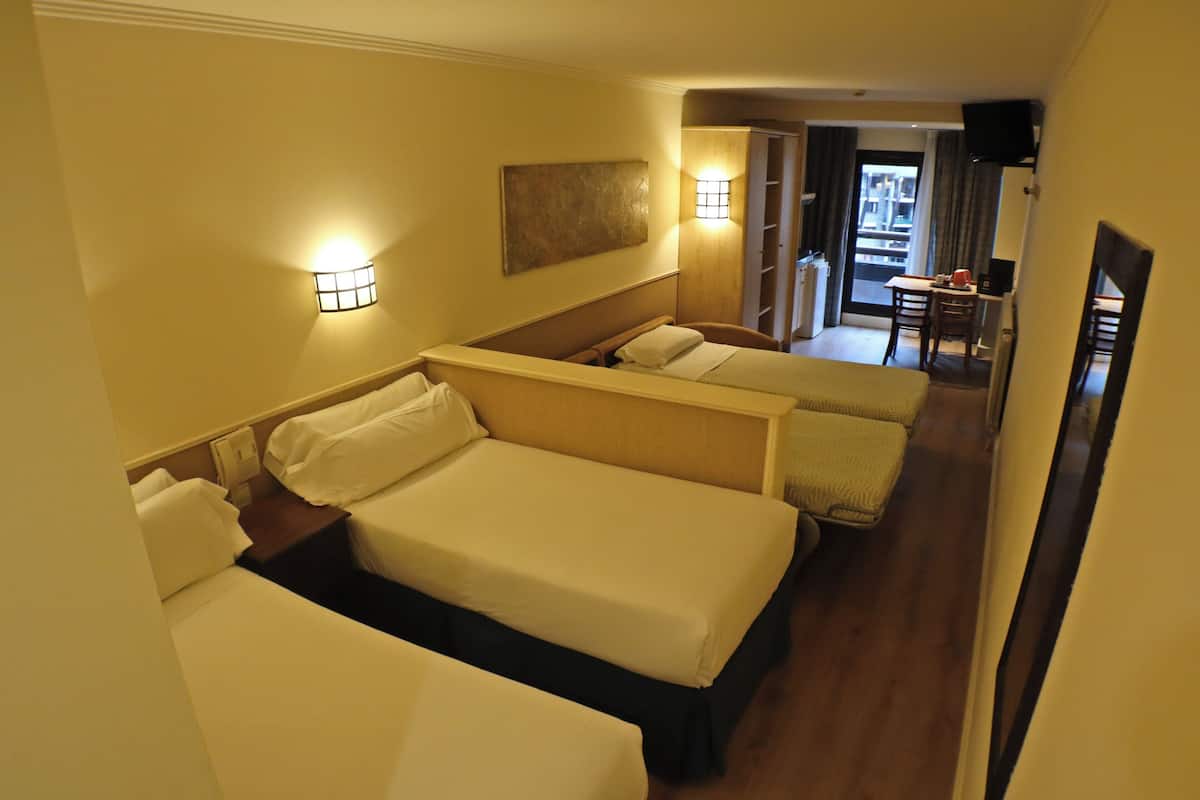 A hotel room with three beds, a desk, and a chair.
