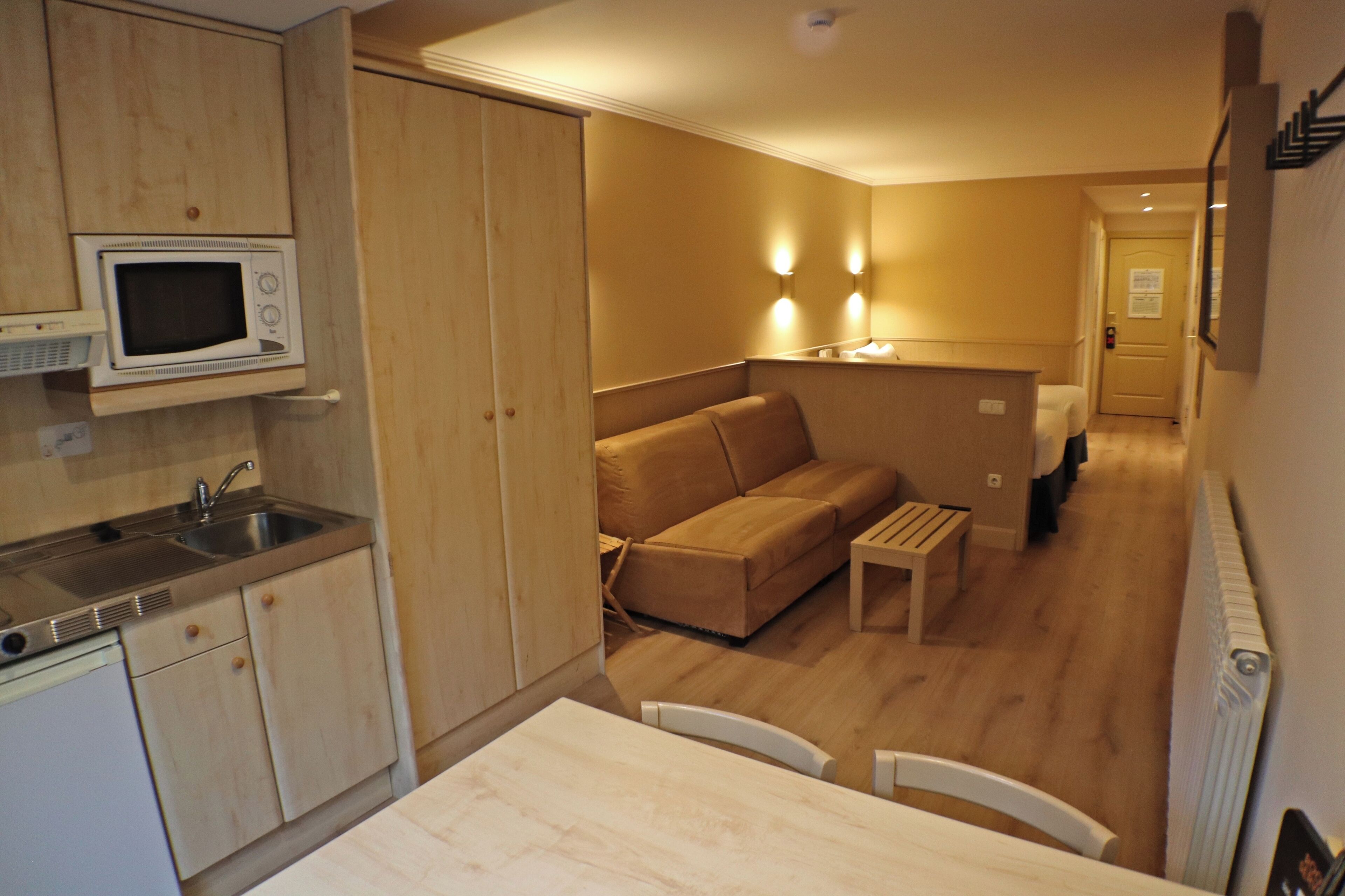Una cocina compacta con microondas, pileta y muebles de madera. Hay una pequeña mesa de comedor con sillas y un sofá en la zona de estar.