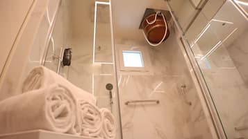A modern shower with a glass door, a handheld showerhead, and a towel rack with neatly rolled towels.