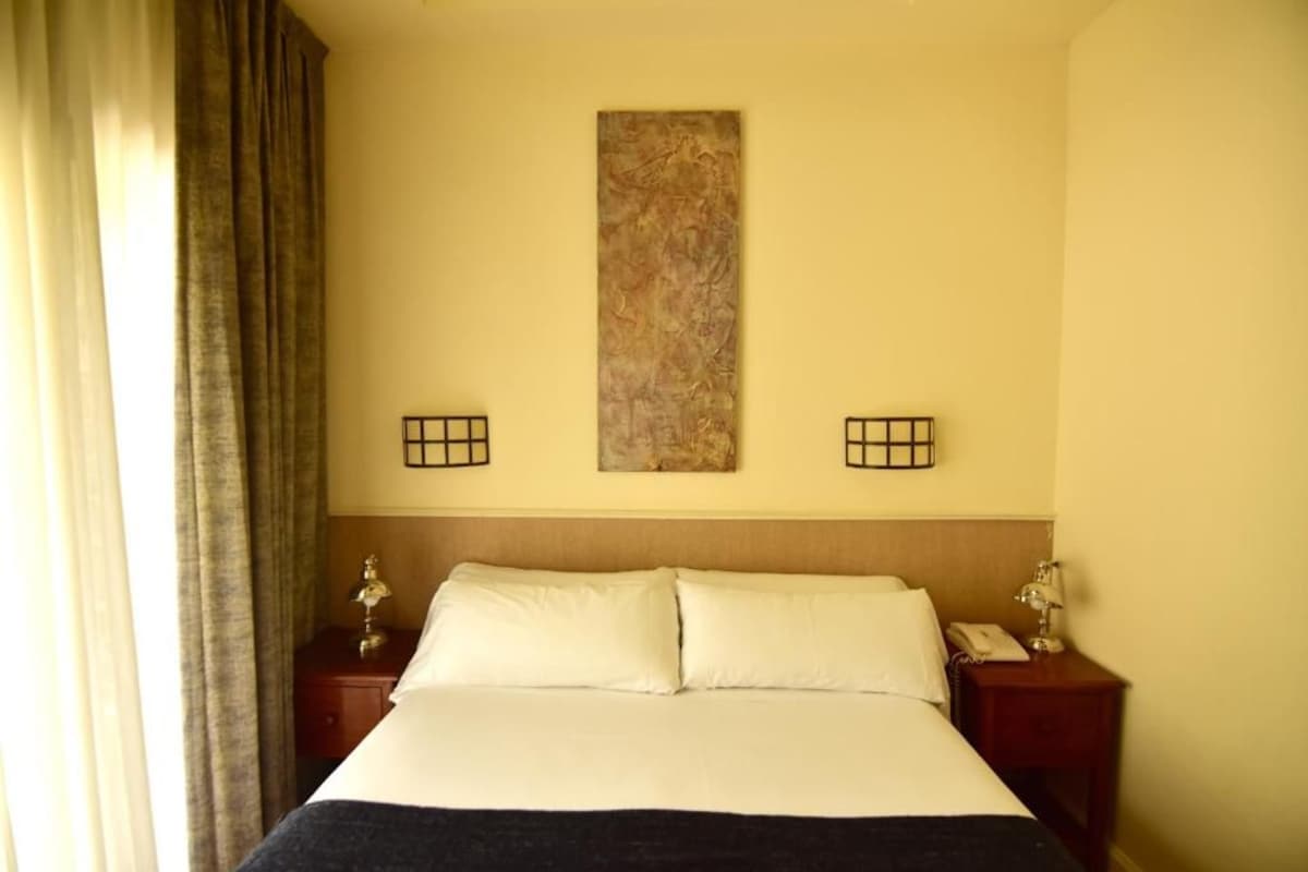 A hotel room with a bed, two bedside tables, a wall-mounted artwork, and a curtain on the left.