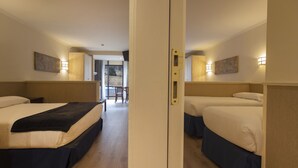 Habitación de hotel con dos camas, suelo de madera y vistas al exterior a través de una puerta.
