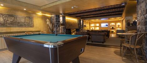 A pool table in a room with a stone wall, a fireplace, and a television.