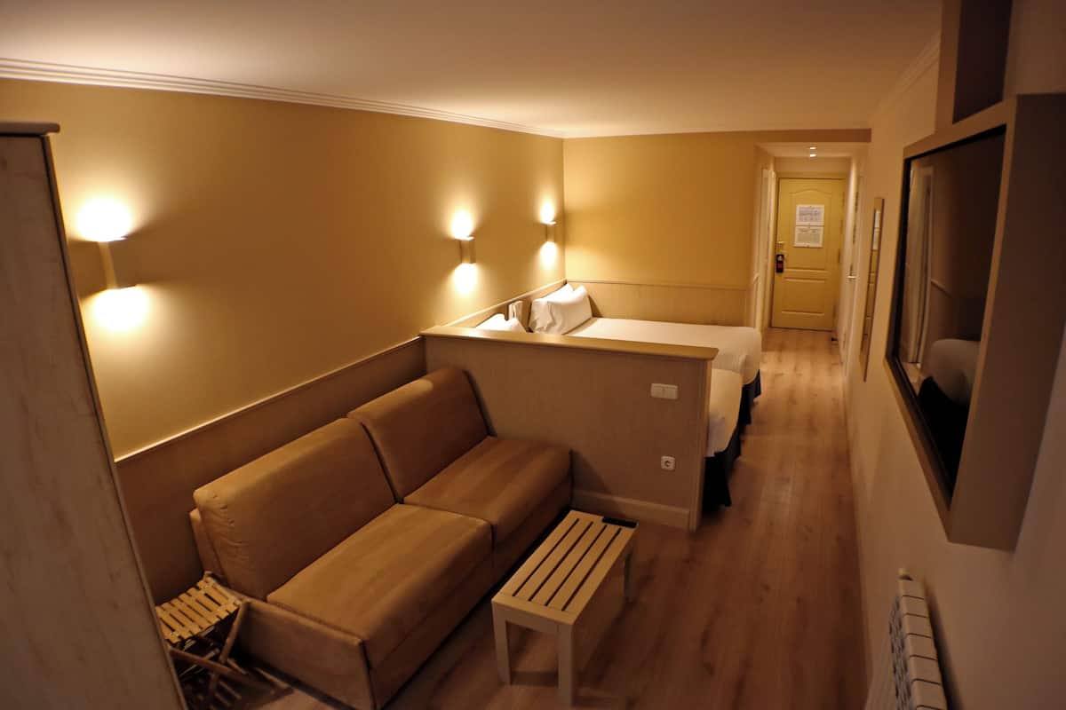 A compact hotel room with a sofa, a small table, and a bed.