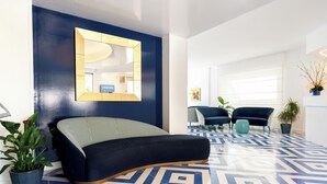 A modern room with a blue and white patterned floor, a black sofa, a large mirror, and two chairs. - La Meridiana (Sorrento)