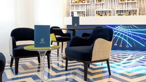 A bar area with a drink list stand, seating with a patterned floor, and a wall with shelves of bottles. - La Meridiana (Sorrento)