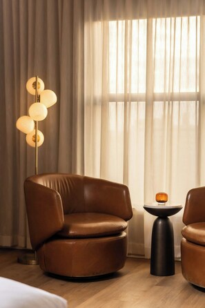 A room with a brown leather chair, a small round table with a candle, and a floor lamp with multiple spherical lights. - Hutton Hotel, Nashville, a Tribute Portfolio Hotel (Nashville)