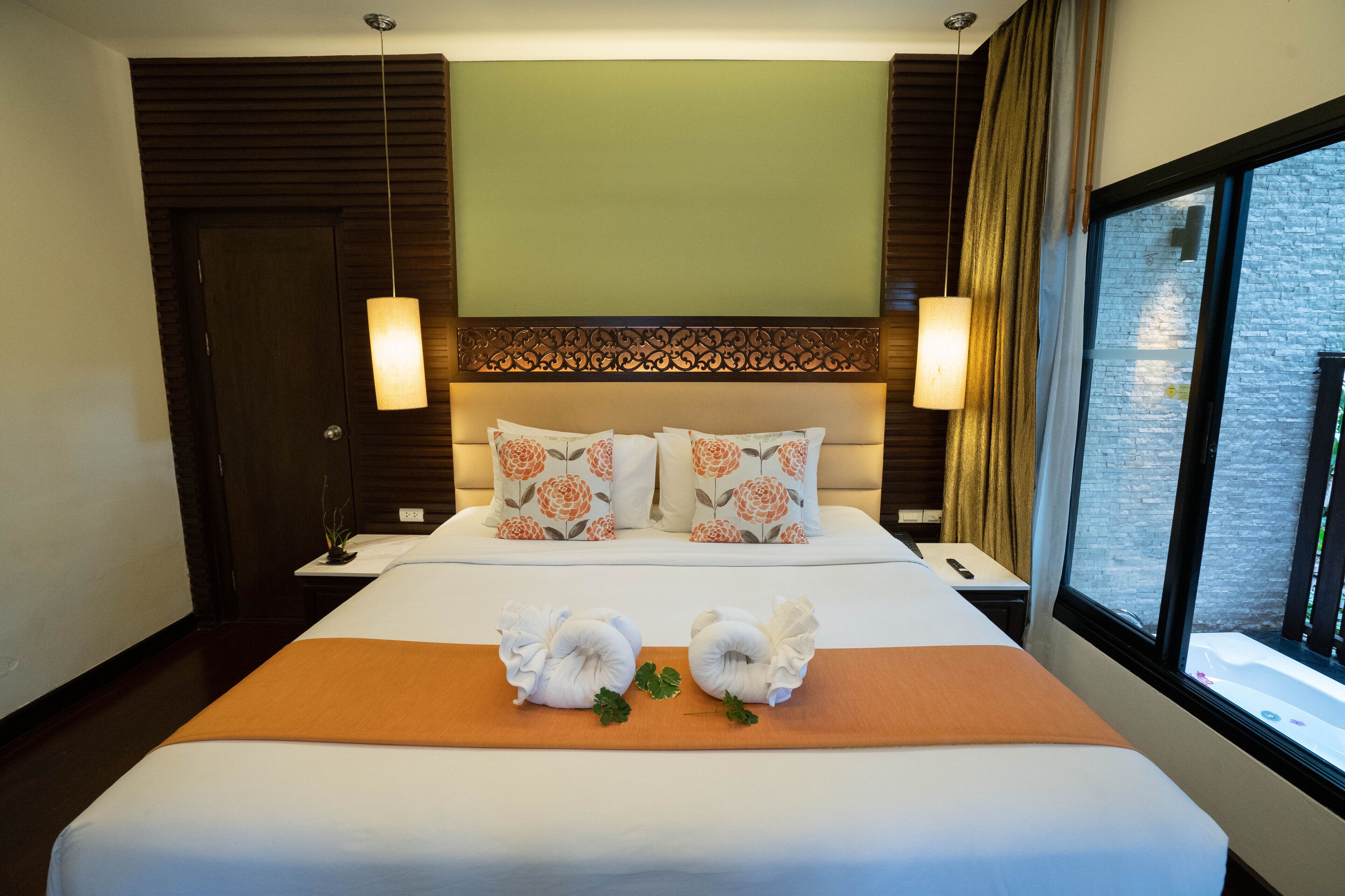 Une chambre d’hôtel avec un grand lit, deux oreillers à motifs floraux, une table de chevet avec une lampe et une fenêtre donnant sur un mur de briques.