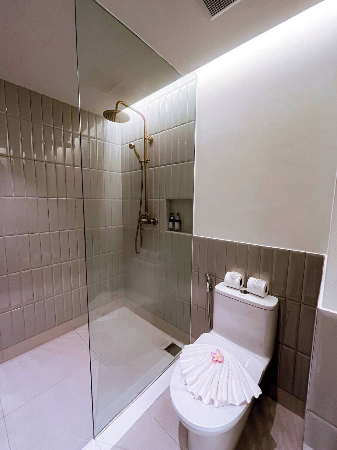 Egy modern fürőszoba üvegfalas zuhanyzóval, egy díszes törölközővel ellátott WC-vel és üveg válaszfallal.