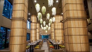 A spacious dining area with multiple tables and chairs, large bamboo columns, and hanging light fixtures. - Peach Hill Resort (Karon)
