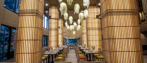 A spacious dining area with multiple tables and chairs, large bamboo columns, and hanging light fixtures.