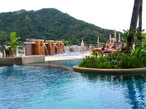 A pool area with a waterfall feature, lounge chairs, and a view of a forested hill.