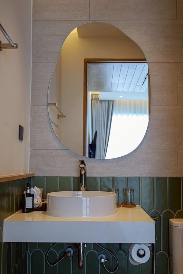 A bathroom with a round mirror, a white sink, and a towel dispenser.