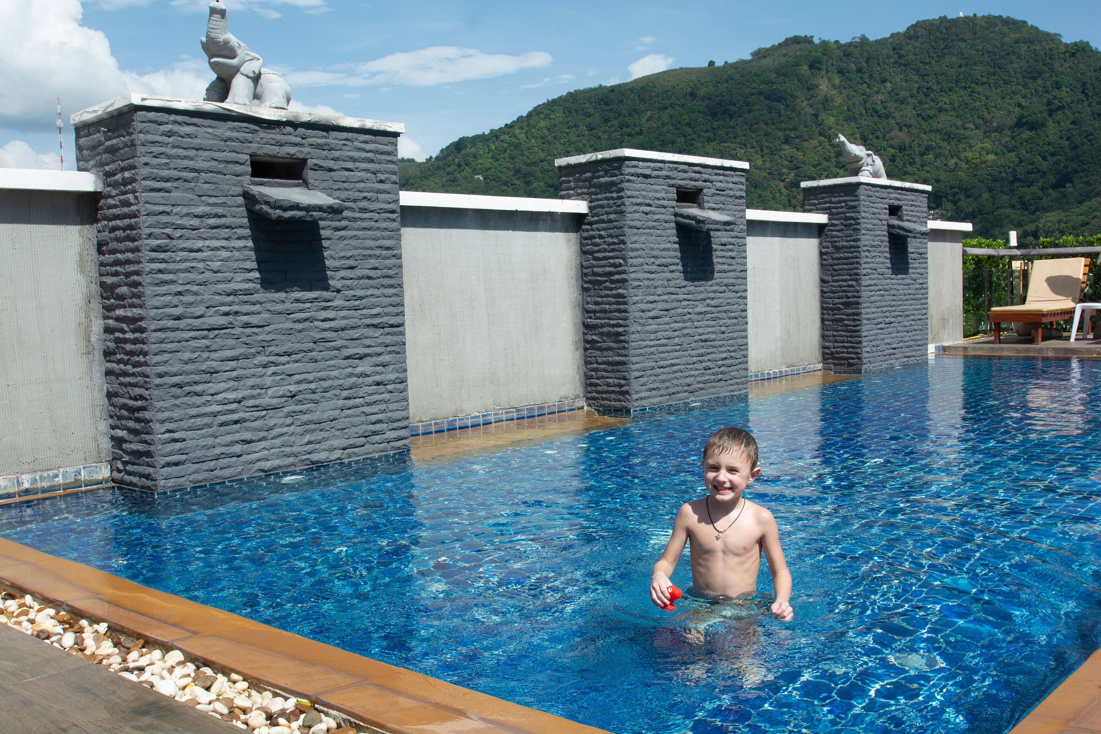 Una piscina con paredes de piedra y un niño jugando en el agua.