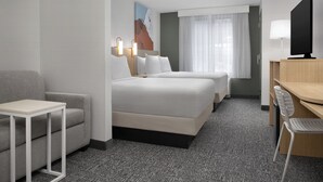 Habitación de hotel con dos camas, un escritorio, una silla, un televisor y un cuadro en la pared.
